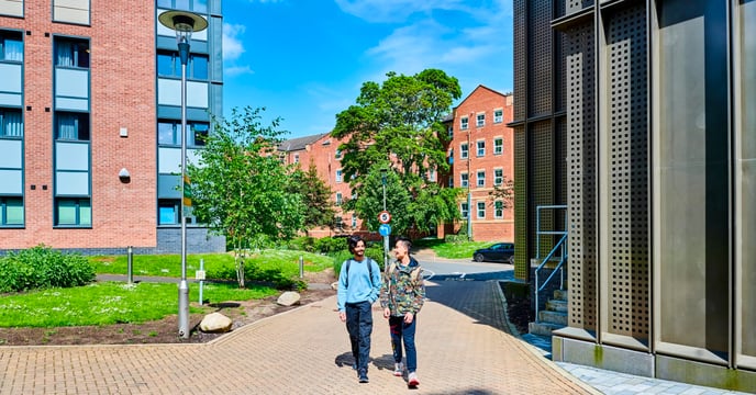 Two students walk through campus between two large buildings.