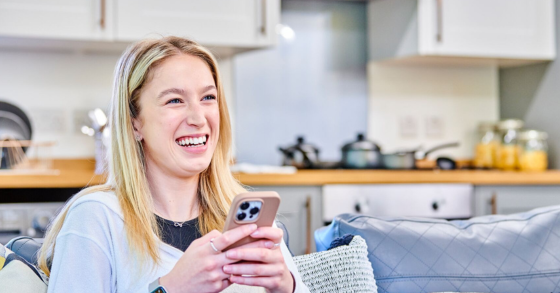 A student sat in her kitchen on her phone, laughing and smiling