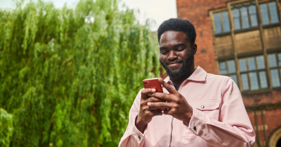 Student walking past Arches smiling at phone