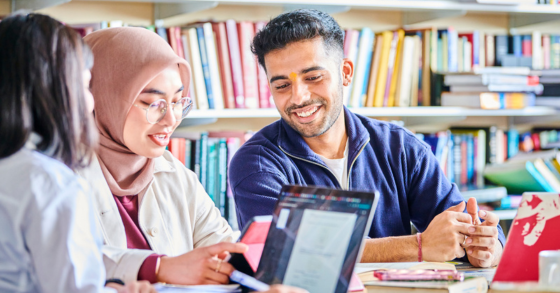 Three students sat studying with books in background