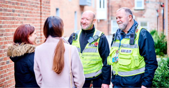 Two University security team smiling and chatting to two students