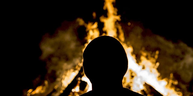 A man looks on at a bonfire