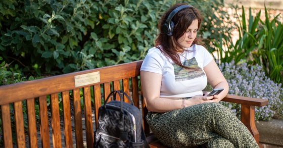 A student on her phone, with headphones, sat on a bench in the Quad