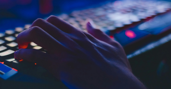 close-up image of hands on a keyboard in a dark room with purple and red lighting 