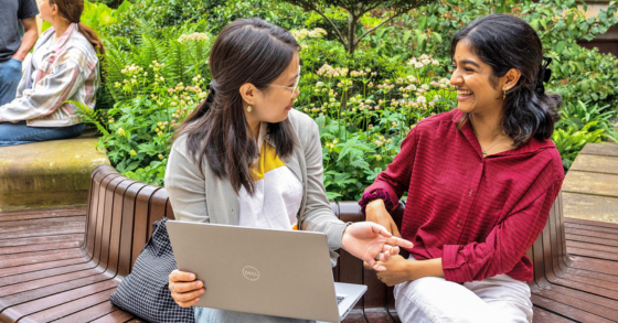 Two students sitting on campus talking about something on a laptop