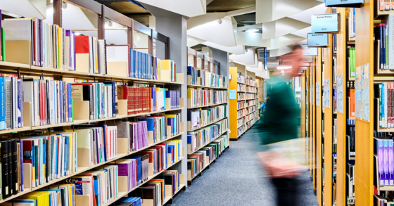 Rows of books in the library with a blurry figure