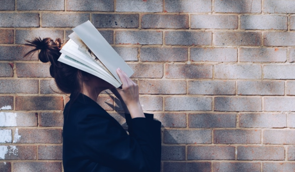 Woman stood in front of brick wall with book covering her face