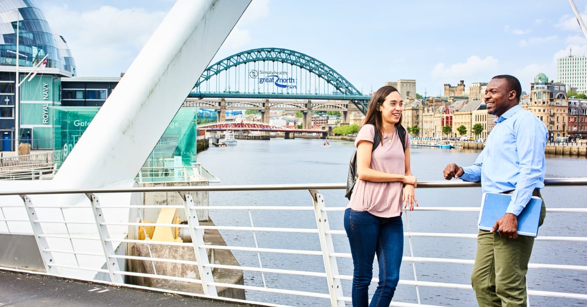 Students stand and talk on the Millennium Bridge in Newcastle, with the Tyne Bridge in the background.