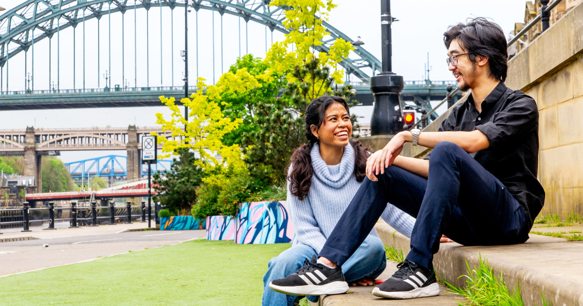 newcastle uni students laughing in front of the tyne bridge