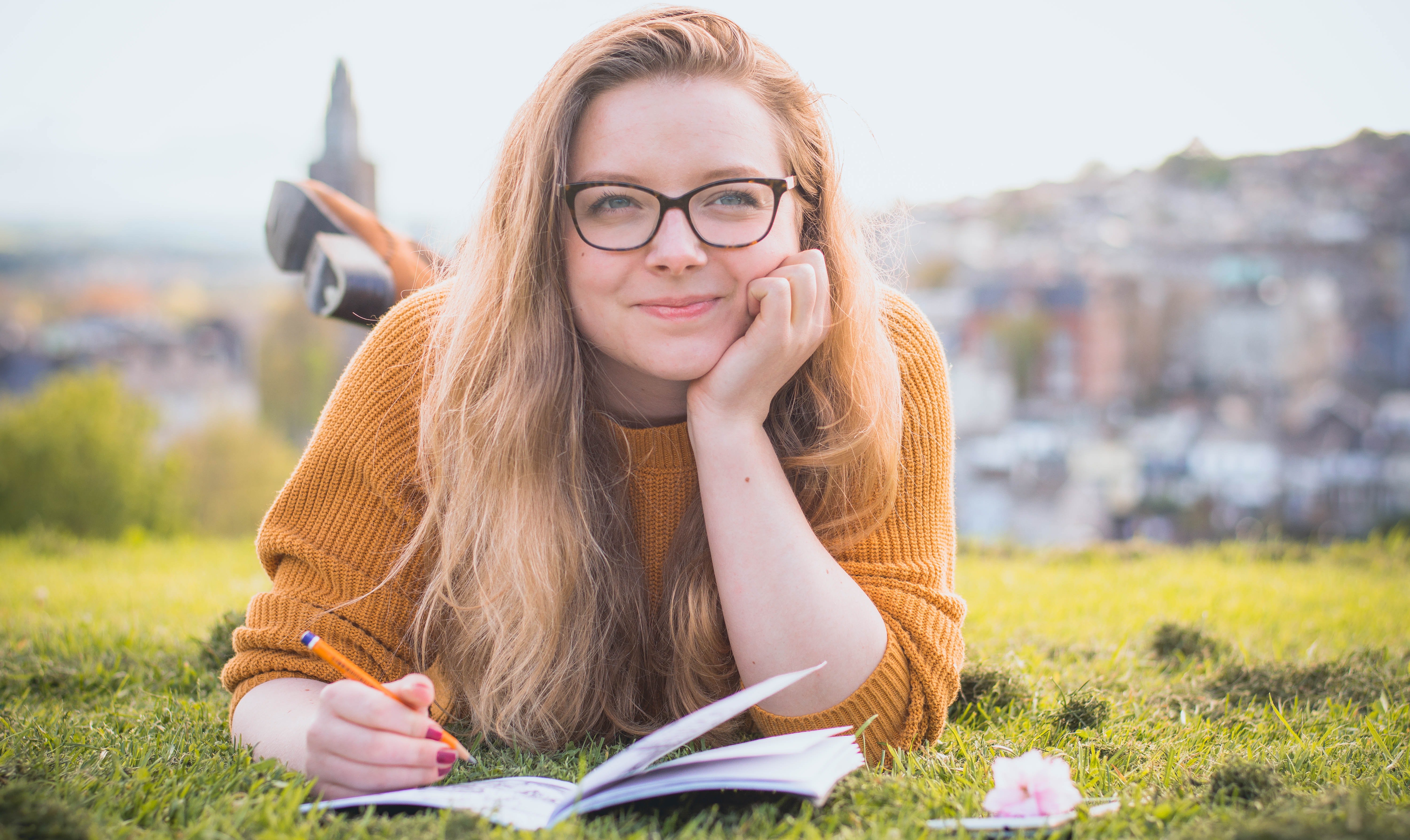 woman-lying-on-green-grass-while-holding-pencil-1458318